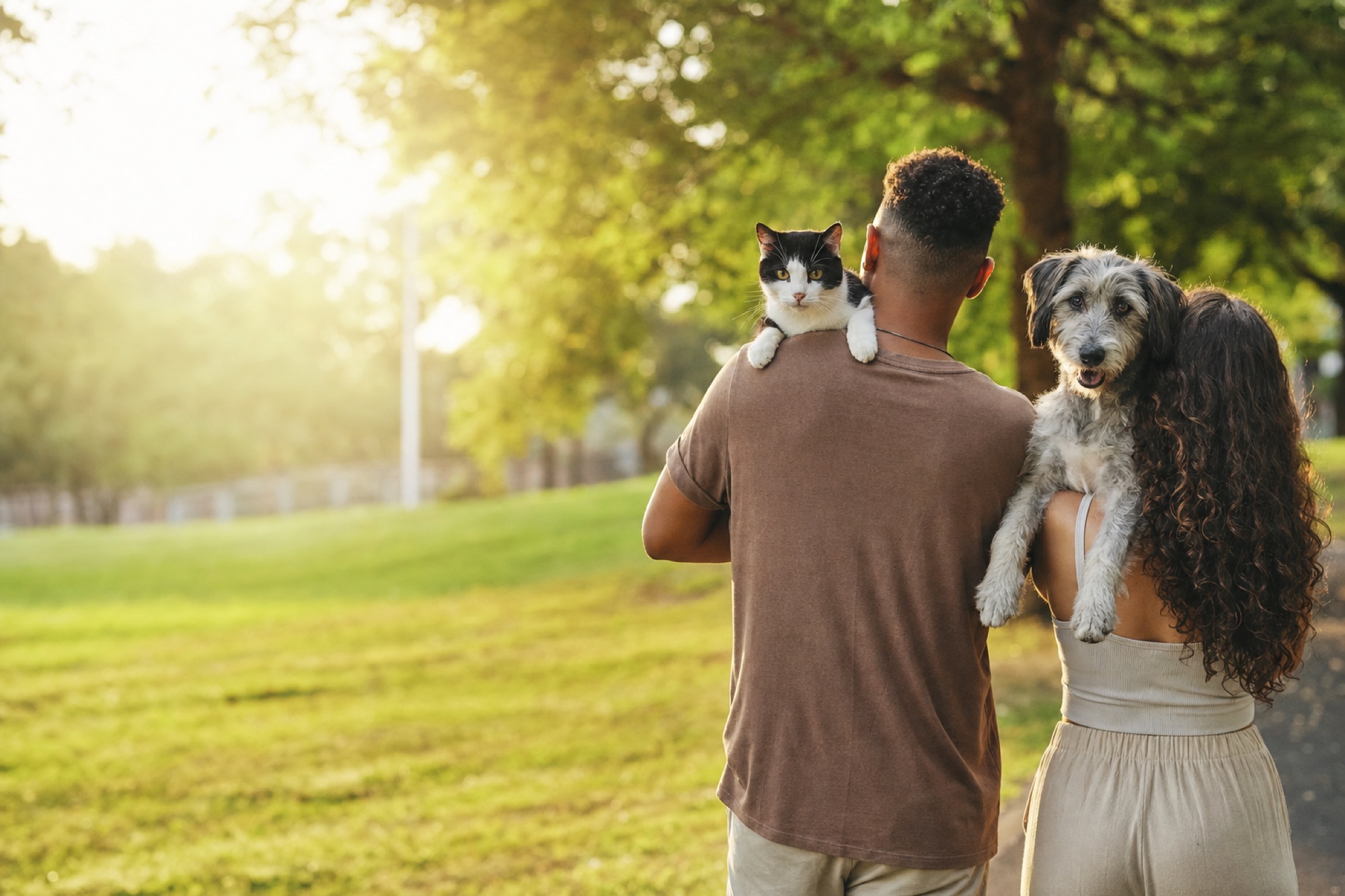 Casal caminhando em um parque, um carregando um gato e o outro um cão no ombro